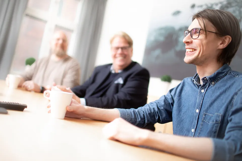 Tre kollegor skrattar tillsammans vid konferensbordet.
