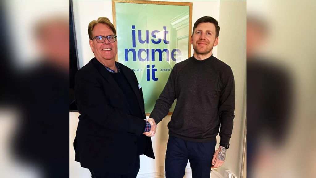 Magnus Johansson och Andreas Olofsson skakar hand framför en affisch med Just Name IT:s logotyp.