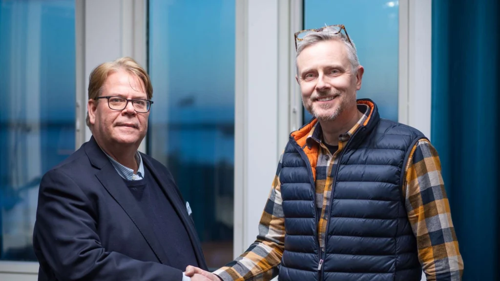 Handslag mellan Magnus Johansson och en representant för Studio Knarr framför ett fönster.