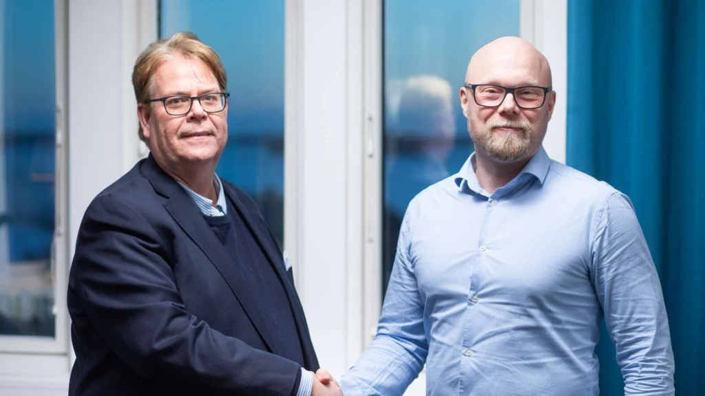 Magnus Johansson och Fredrik Ryttersson skakar hand framför ett fönster.