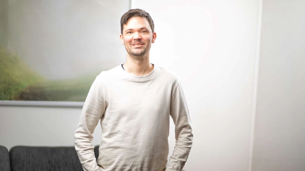 Robin Öhrman i ljus tröja står med händerna i fickorna på kontoret.