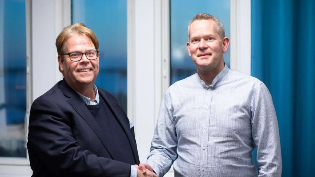 Magnus Johansson och Linus Linné skakar hand framför ett fönster.